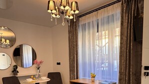 Una camera moderna con zona pranzo, un piccolo tavolo con sedie, uno specchio e un'ampia finestra con tende.