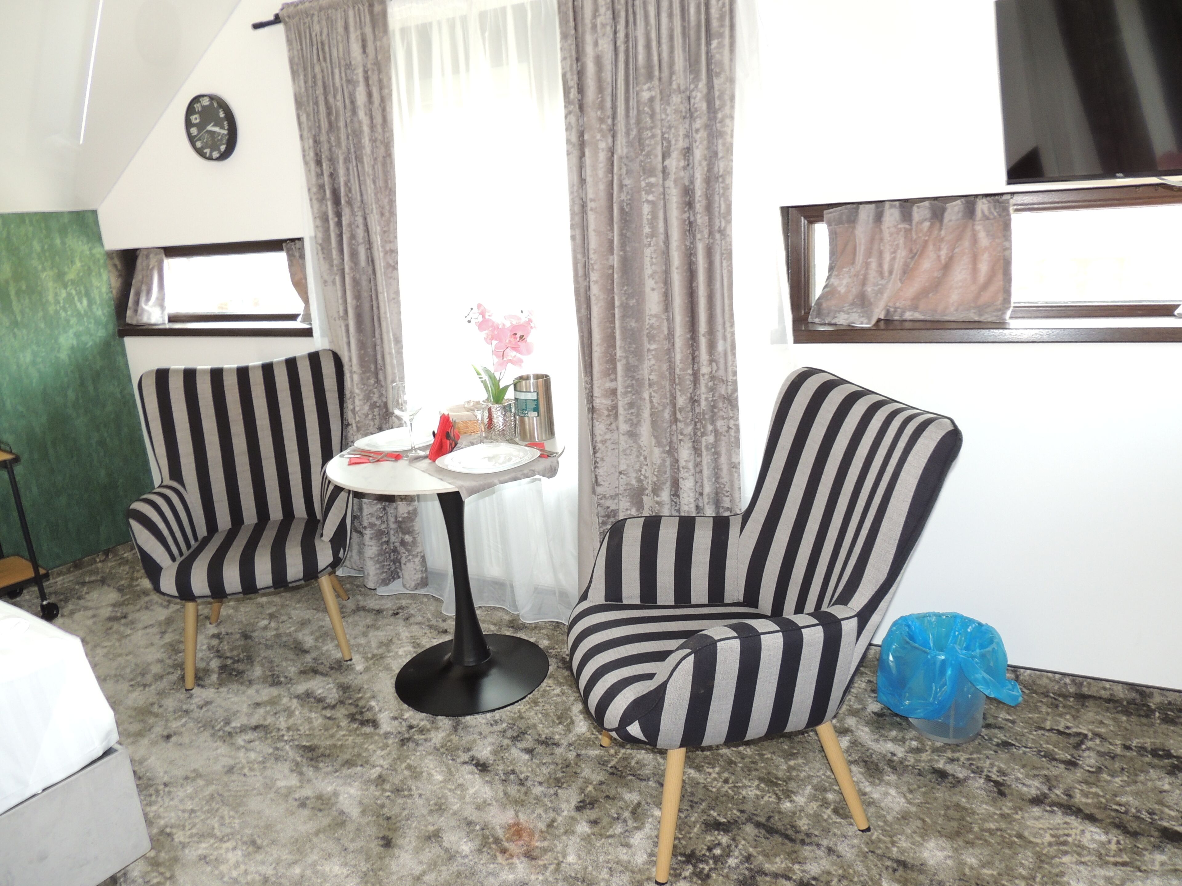 Una habitación con dos sillones a rayas, una mesita redonda con mantel blanco y una cama.