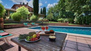 A poolside setting with a table set with fruits and drinks, a pool, and a brick house in the background. - Giunchette Meri, Cavriglia, Arezzo and Cortona (Cavriglia)