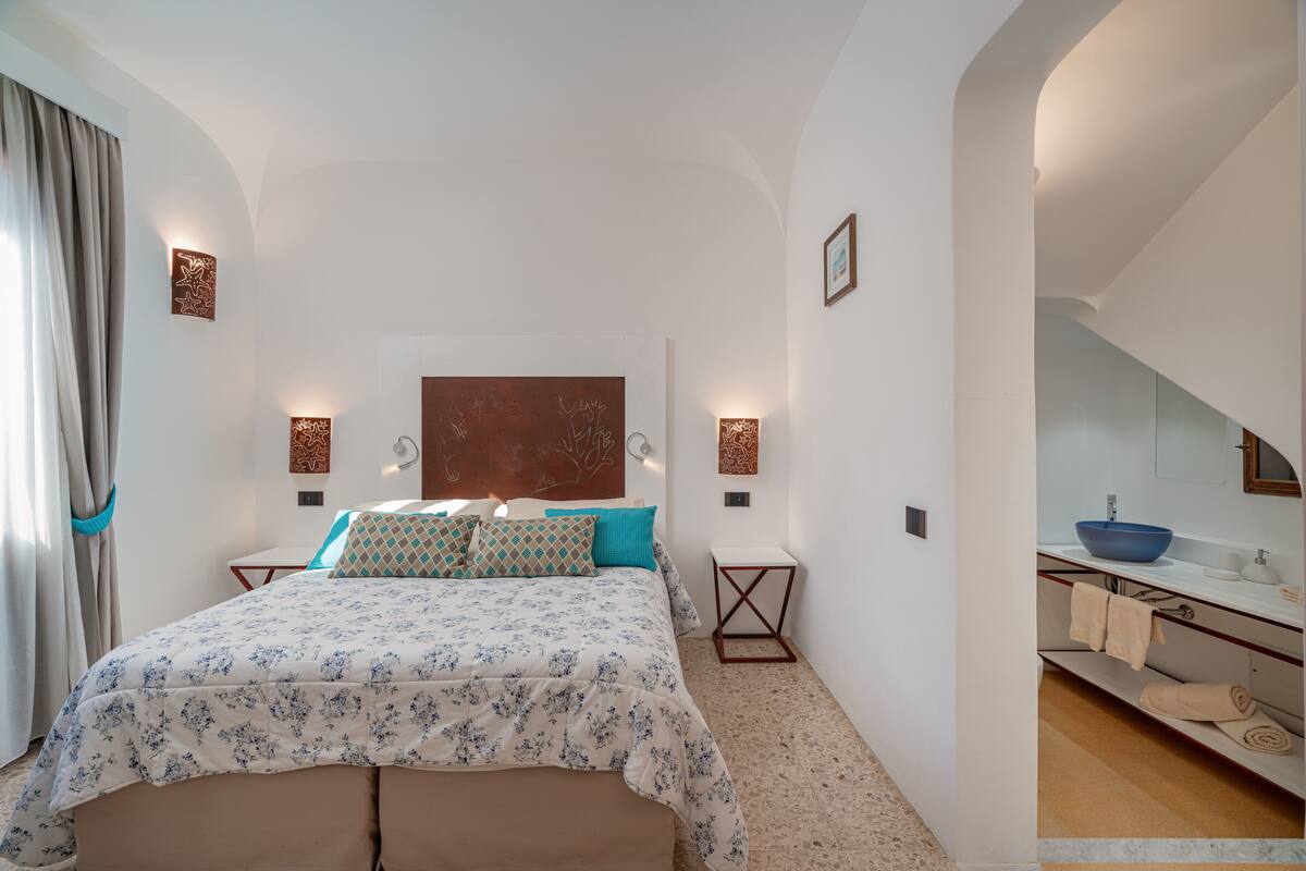 Une chambre à coucher comprenant un lit, des tables de chevet, une commode, une tête de lit et une salle de bain avec un lavabo et un miroir.