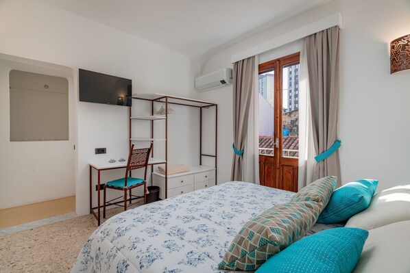 Une chambre à coucher avec un lit, un bureau, une chaise, un téléviseur et une fenêtre avec des rideaux.
