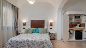 Une chambre à coucher comprenant un lit, des tables de chevet, une tête de lit, un four à micro-ondes encastré et un petit réfrigérateur.