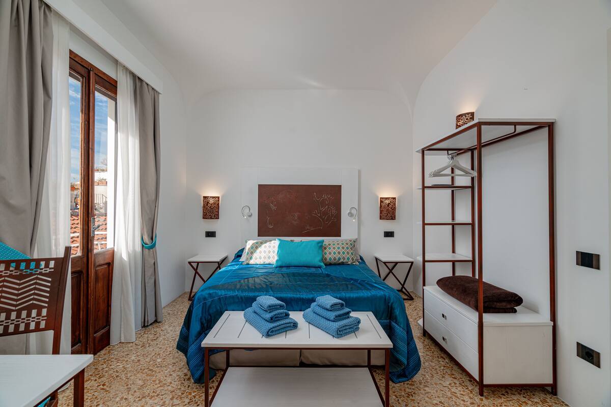 Une chambre à coucher avec un lit, des tables de chevet, une étagère suspendue et une vue sur l’extérieur.