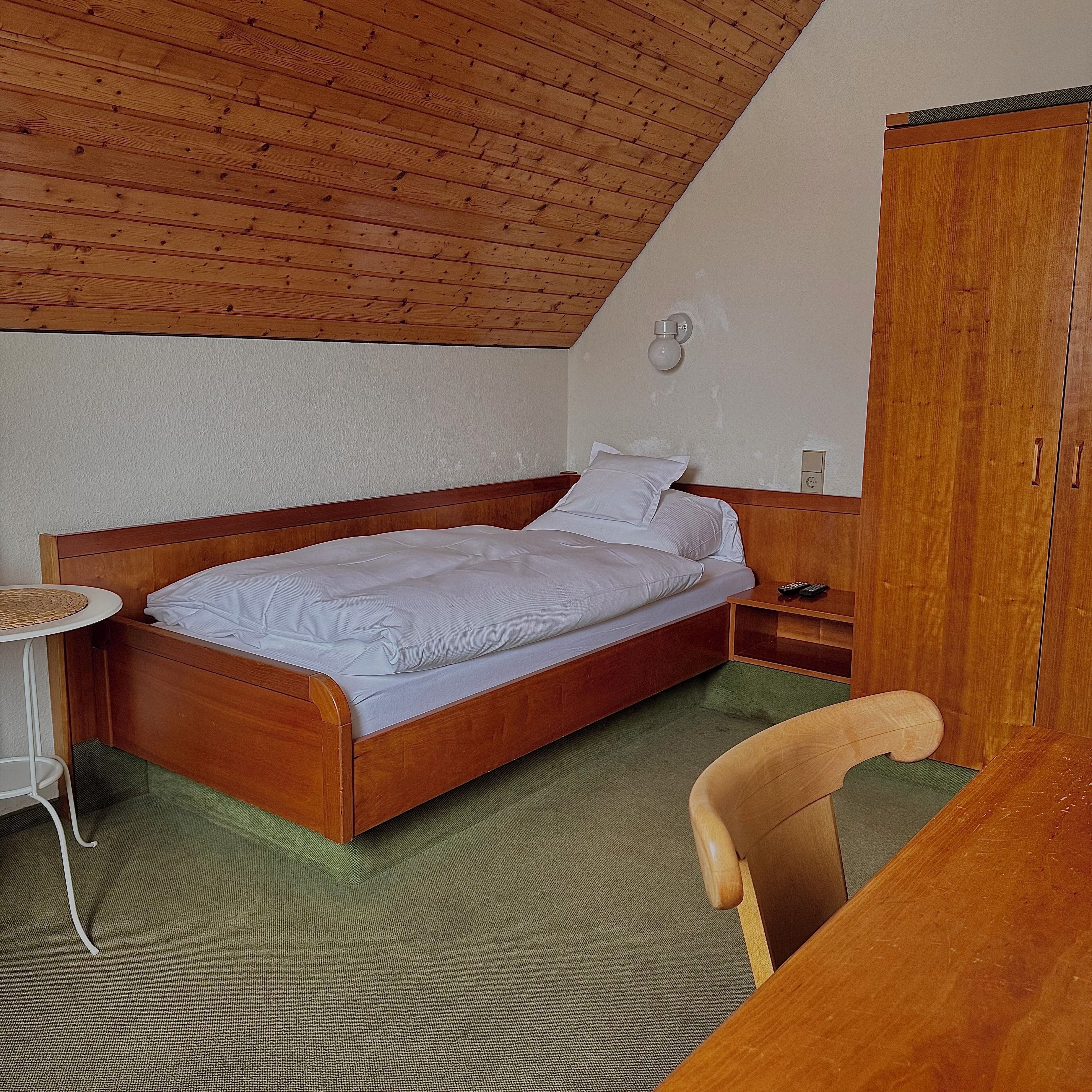 A bedroom with a wooden bed, a bedside table, a chair, and a wardrobe.