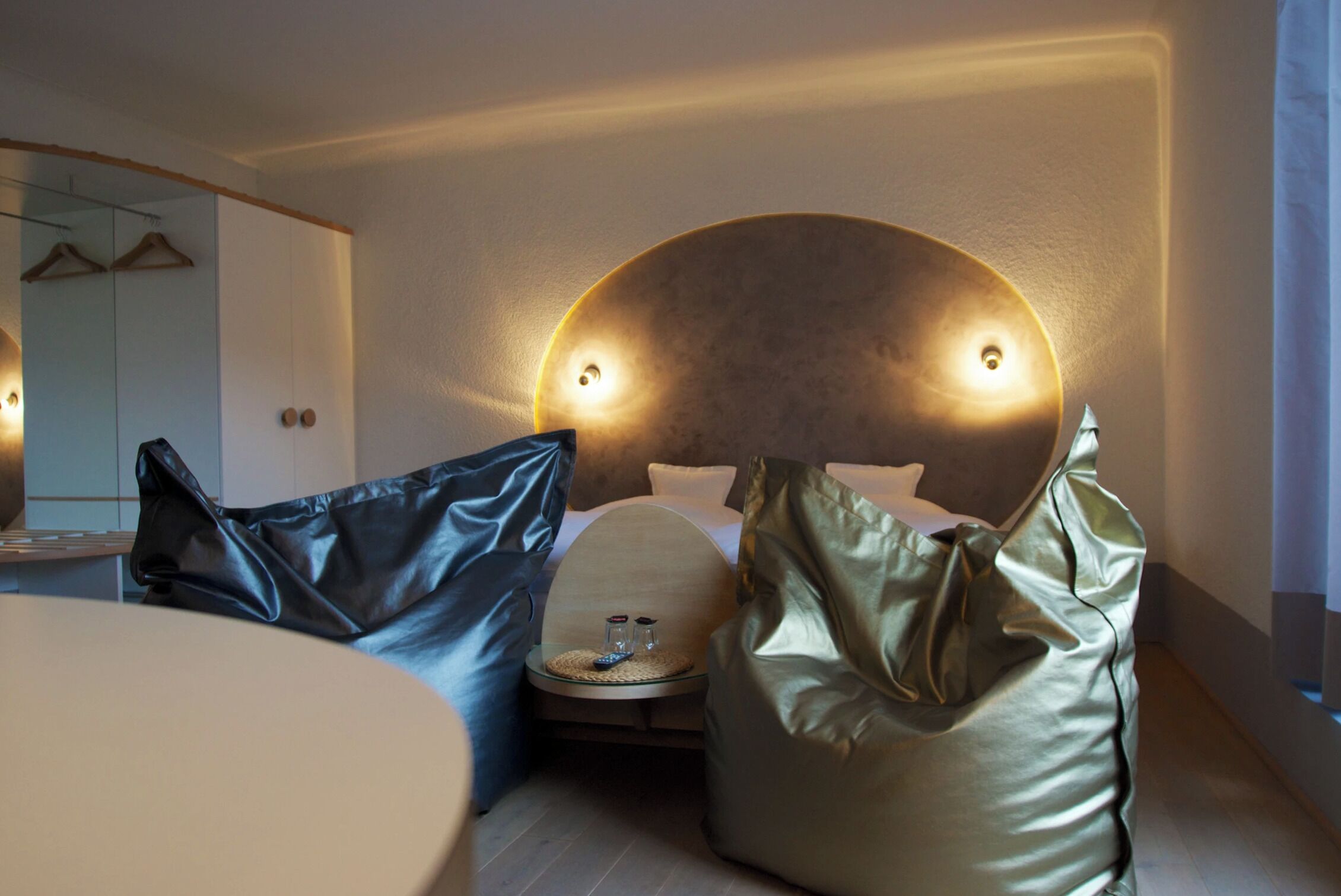 Een moderne hotelkamer met een gebogen hoofdeinde, een rond nachtkastje en een grote spiegel.