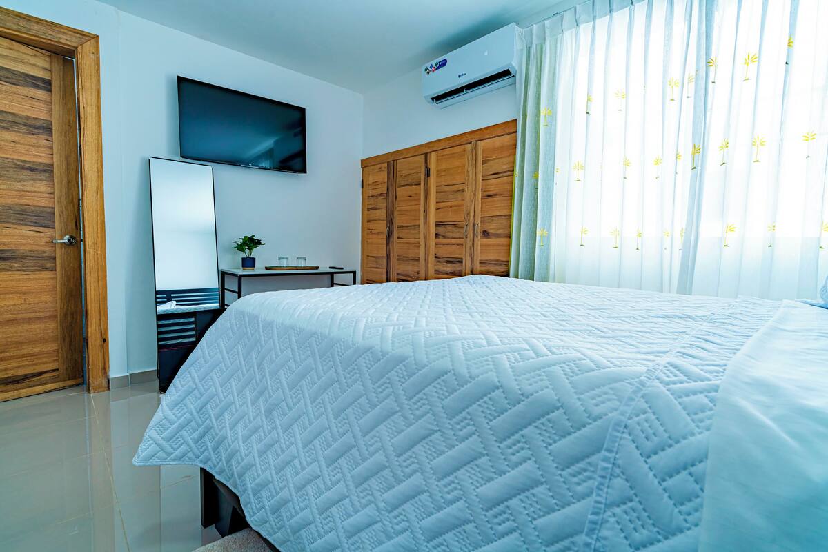 Un dormitorio con una cama, un televisor montado en la pared, un armario y un equipo de aire acondicionado.