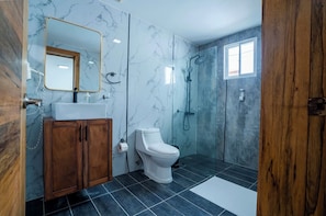 A bathroom with a marble wall, a wooden cabinet, a toilet, a sink, and a shower area.