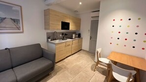 Ett kompakt bostadsutrymme med en soffa, ett matbord med stolar, en liten köksdel och en vägg med färgglada prickar.