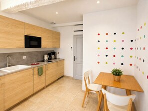 A modern kitchen with wooden cabinets, a black microwave, and a coffee machine. There is a dining area with a wooden table and two chairs. - Holiday in Arles: Amphitheatre Apartment A (Arles)