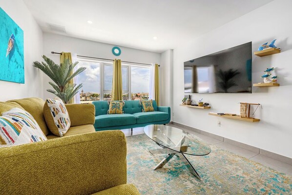 A modern living room with a teal sofa, a yellow armchair, and a glass coffee table.