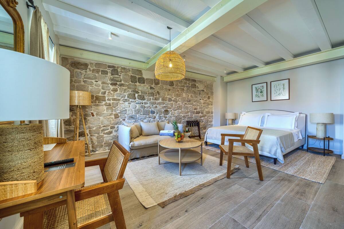 Una habitación acogedora con pared de piedra, una cama, un sofá, una mesa de comedor y una lámpara colgante.