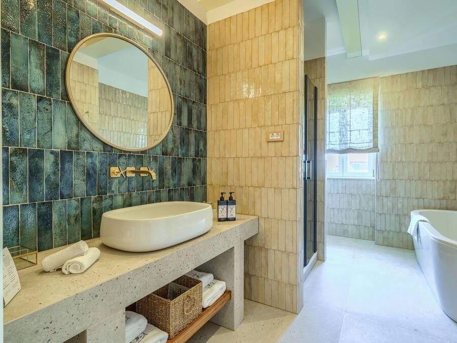 Un baño con un espejo ovalado grande, un lavamanos y una bañera. Hay toallas y artículos de aseo en la encimera.
