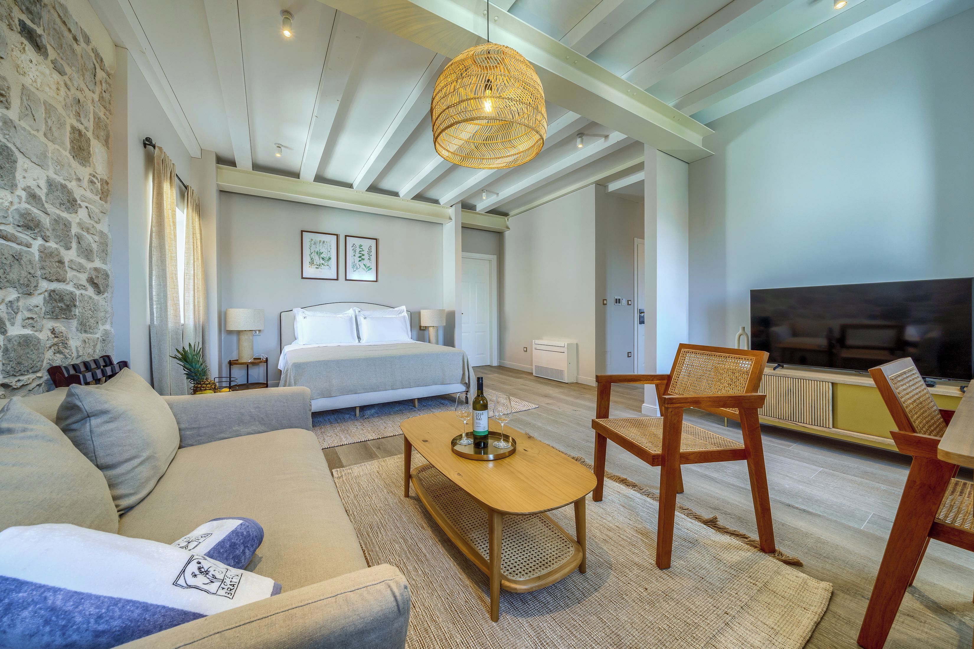 Een moderne hotelkamer met een stenen muur, een bed met witte lakens, een houten bijzettafeltje en een grote televisie.