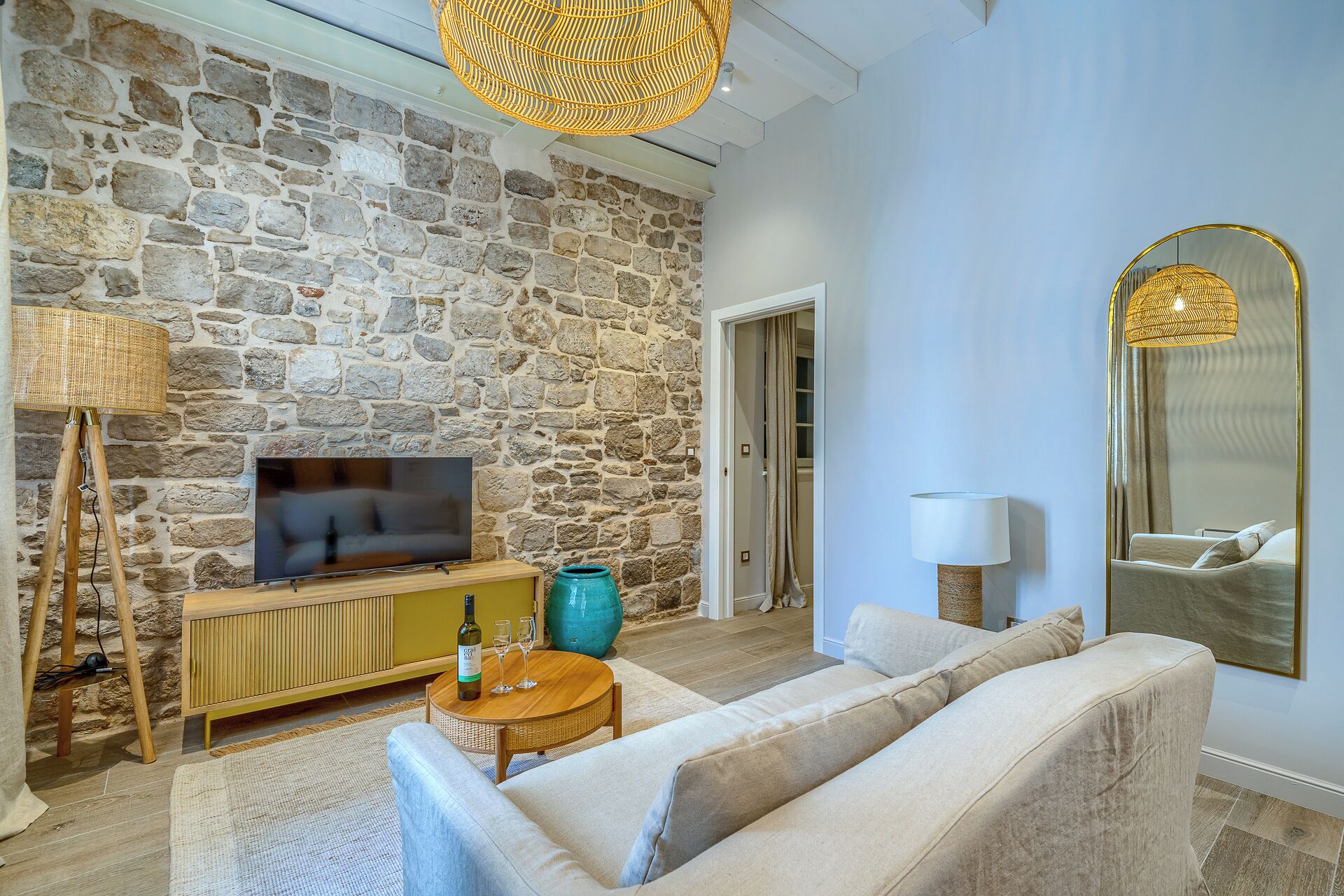 Un salon avec un mur en pierre, un téléviseur, un canapé, une table basse et une lampe.