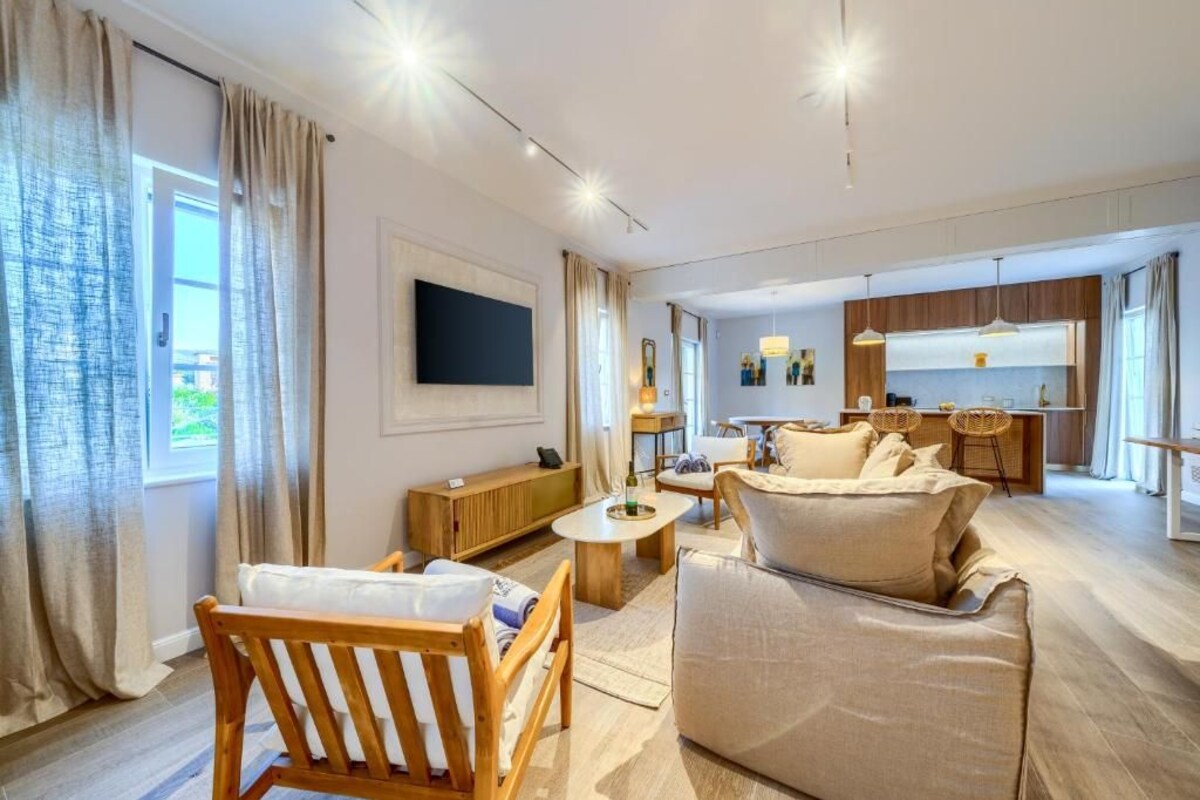 A modern living room with a sofa, armchair, and coffee table. There is a kitchen area with a dining table and chairs.