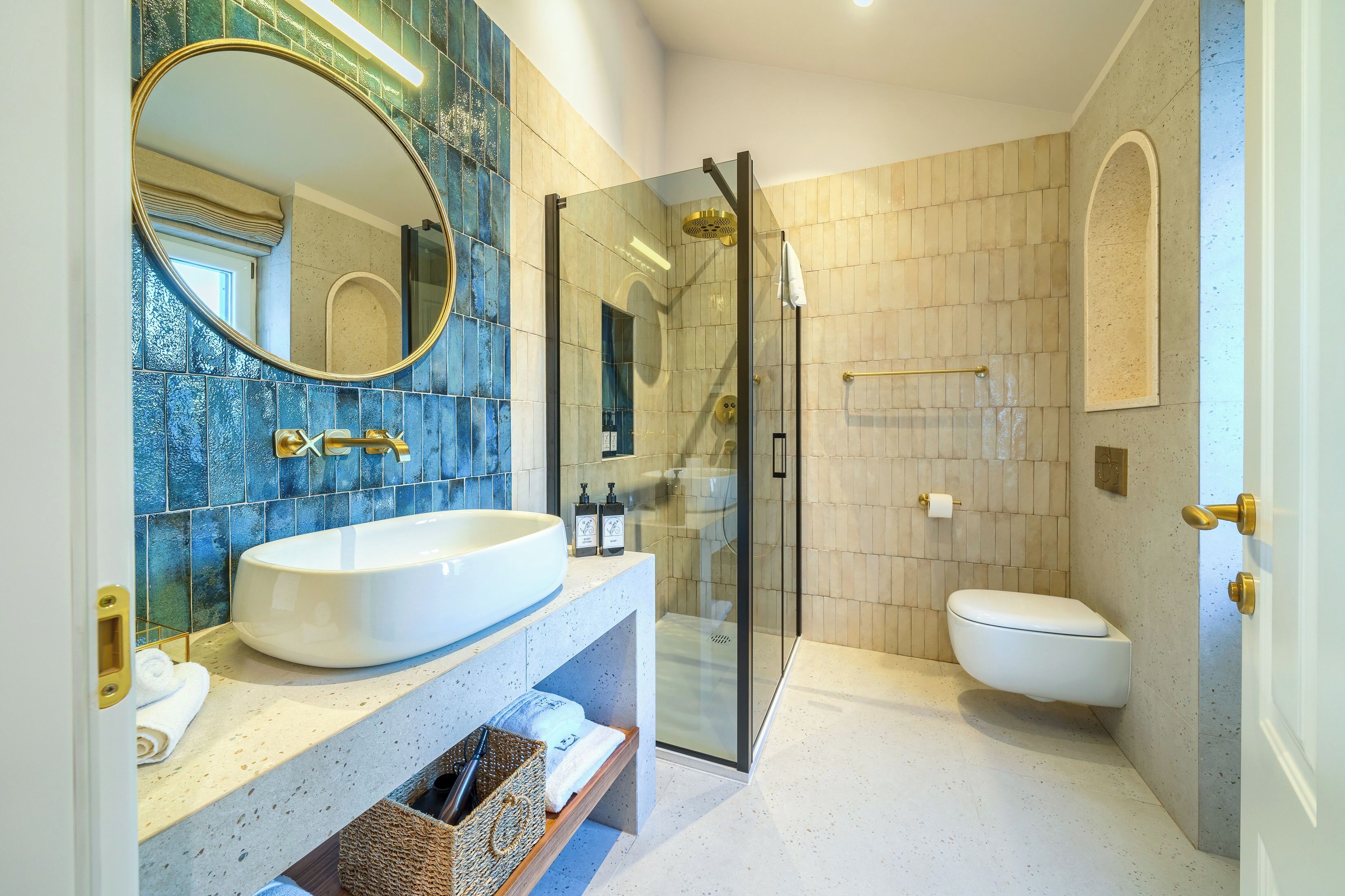A modern bathroom with a large oval mirror, a white sink, a glass-enclosed shower, and a toilet.