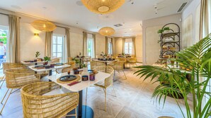 A spacious dining area with wicker chairs, round tables, and pendant lighting. - Hotel Brattia (Postira)