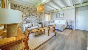 A room with a stone wall, a bed, a sofa, a wooden table, and a hanging light fixture. - Hotel Brattia (Postira)