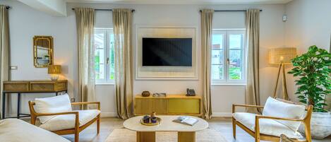Une chambre d’hôtel équipée d’une grande télévision, de deux fauteuils, d’une petite table, d’un bureau et d’une grande plante en pot.