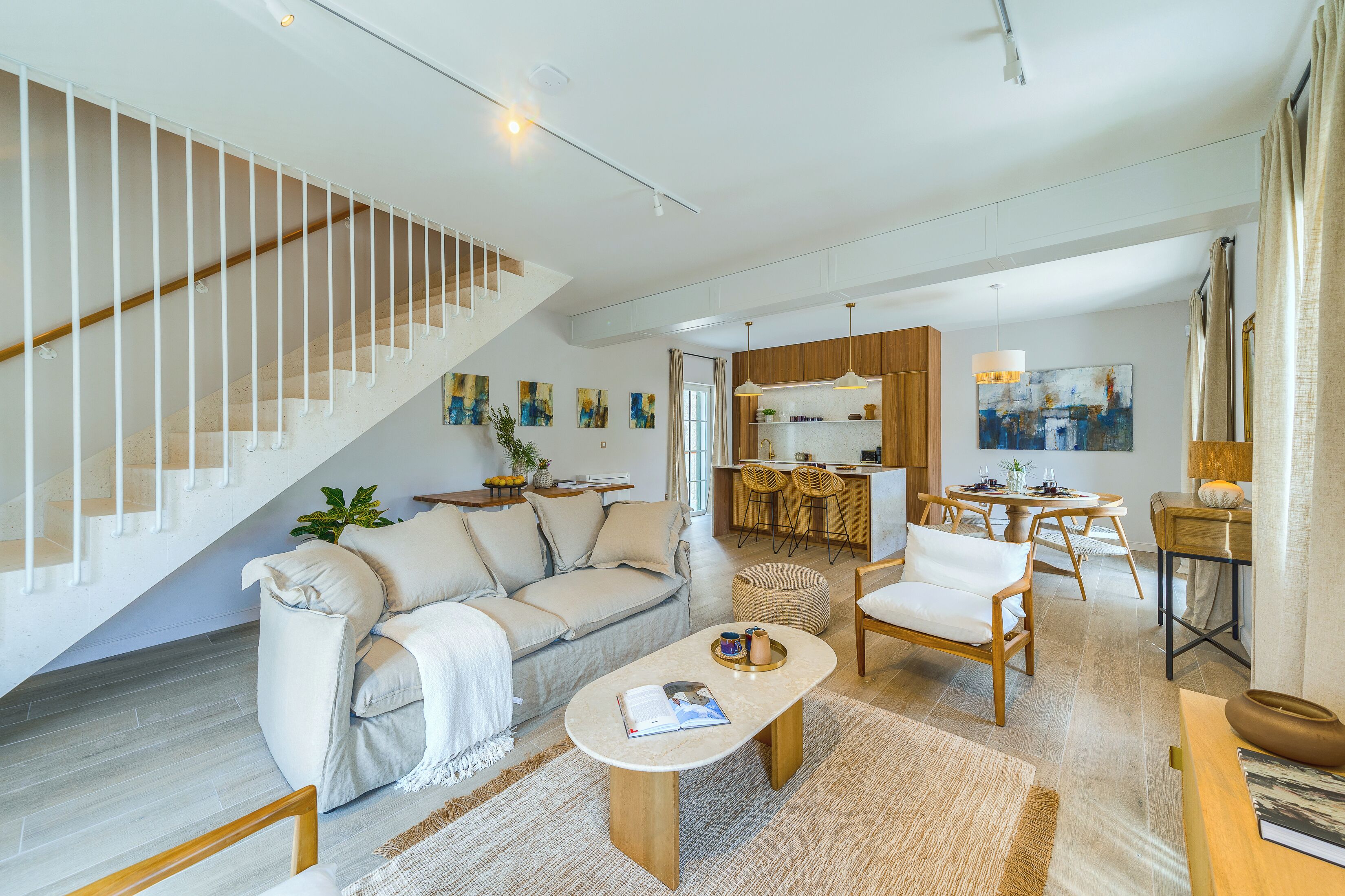 Een ruime woonkamer met een trap, een bank, een salontafel en een eethoek met stoelen en een tafel.