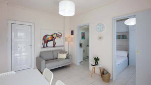 Una sala de estar moderna con un sofá, una mesa de comedor, una lámpara de techo blanca y una obra de arte de un elefante colorido.