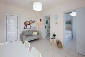 A modern living room with a sofa, a dining table, a white ceiling light, and a colorful elephant artwork.