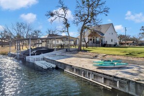 A dock with boats, a covered area, and a white house with a sloped roof.
