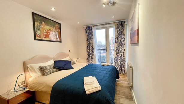A hotel room with a bed, a painting, a window with curtains, and a view of the outside.