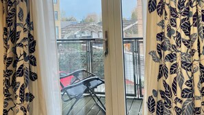 A room with a large sliding glass door leading to a balcony. The room has a bed and a chair.