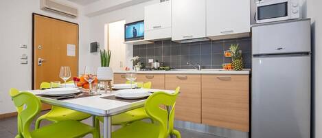 A modern kitchen with white cabinets, a stainless steel refrigerator, and a dining area with a table and bright green chairs.