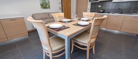 Una cocina moderna con una mesa de comedor para cuatro personas, armarios de madera clara y un suelo de baldosas grises.
