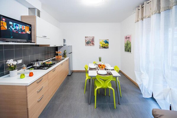 Una cocina moderna con comedor, que incluye un televisor, armarios de madera y sillas de color verde brillante.