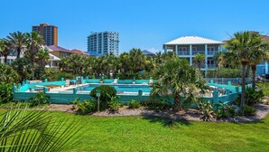 A pool area with multiple lounge chairs and a small pool, surrounded by palm trees and a building with a white facade. - 🌅Community Pool-Walk 2 Beach-Covered Balcony-Pier-2BR Deepwater Cove 103🌅 (Pensacola Beach)