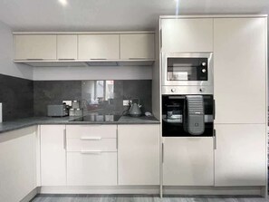 A modern kitchen with white cabinets, a built-in microwave, and a coffee machine.