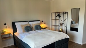 Ein modernes Schlafzimmer mit einem dunkelbraunen Bett, weißer Bettwäsche und zwei Nachttischen mit Lampen.