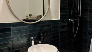 Ein modernes Badezimmer mit rundem Spiegel, Waschbecken in Weiß, einer Seifenspender und einer Dusche mit Duschbrause.