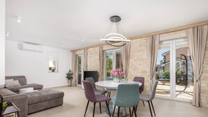 A modern living room with a grey sofa, a round dining table with chairs, and a large window with curtains. - Family Villa Di with pool (Malinska)