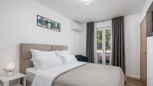 A bedroom with a bed, a bedside table, a lamp, a chair, a window with curtains, and an air conditioning unit. - Family Villa Di with pool (Malinska)