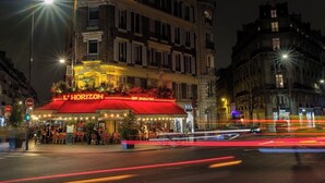 A brightly lit restaurant named 'L'Horizon Bar Brasserie' with outdoor seating and a red awning. - LUXE- A PERFECT BLEND OF CHARM, COMFORT & MODERNITY SAINT GERMAIN- RUE DE RENNES (Paris)