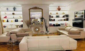 Uma sala de estar moderna com lareira, um espelho grande e uma estante repleta de livros e objetos decorativos.