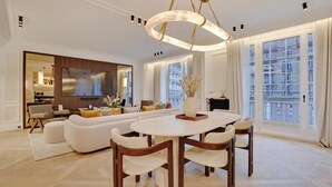A spacious living room with a large sofa set, a dining table with chairs, and a modern chandelier. - LUXE- A PERFECT BLEND OF CHARM, COMFORT & MODERNITY SAINT GERMAIN- RUE DE RENNES (Paris)