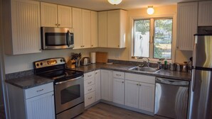 Una cocina con gabinetes blancos, electrodomésticos de acero inoxidable, encimera de granito y una ventana con vistas.