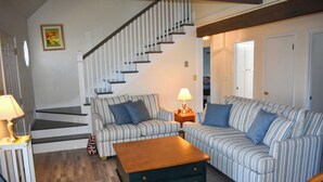 Una sala de estar con sofás a rayas, una mesa de centro de madera, una escalera y una lámpara.