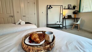 Ein Hotelzimmer mit zwei Betten, einem Schreibtisch mit einem Laptop, einem Stuhl und einem Tablett mit Croissants und einer Tasse.