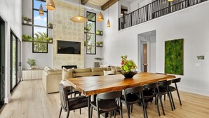 Amplia sala de estar con una mesa de comedor de madera, sillas negras, un sofá beige y un ventanal grande.