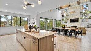 Una cocina amplia con una isla central, ventanas grandes y un comedor con sofá y televisor.