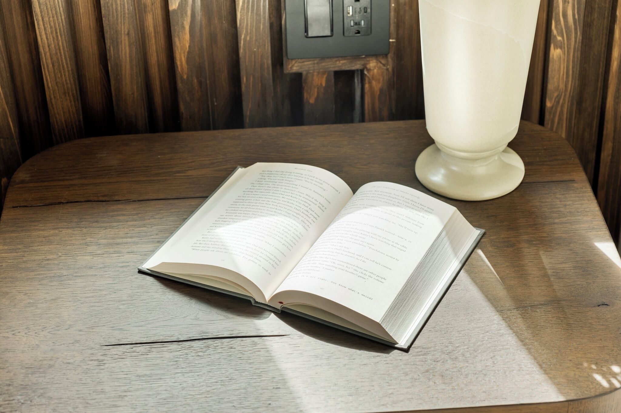 Een open boek op een houten tafel, met een witte lamp op de achtergrond.