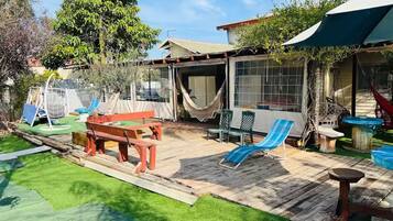 Un patio trasero con una terraza de madera, una hamaca, un conjunto de columpios y un área de patio techada.