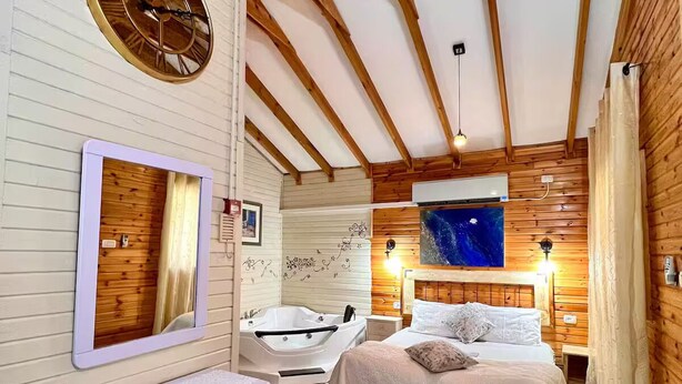 A wooden-paneled bedroom with a large bed, a built-in bathtub, a clock, and a mirror. - Comfort in the center of Upper Galilee, Pets are welcome, with green, spacious. (Mishmar HaYarden)