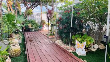 Una terraza de madera que conduce a un jardín con diversas plantas en macetas y una escultura de mariposa.